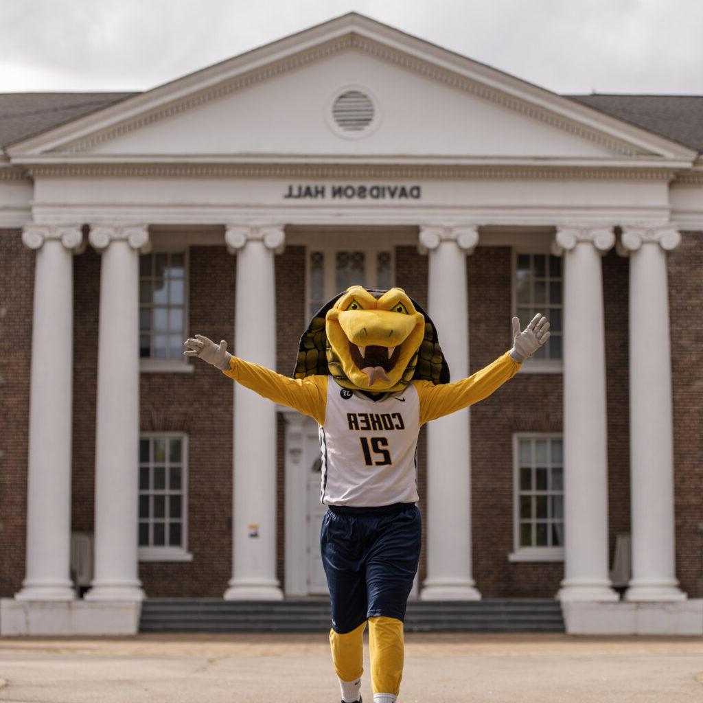 Coker Cobra's Mascot Striker the Cobra poses in front of Davidson Hall with his arms stretched out. 